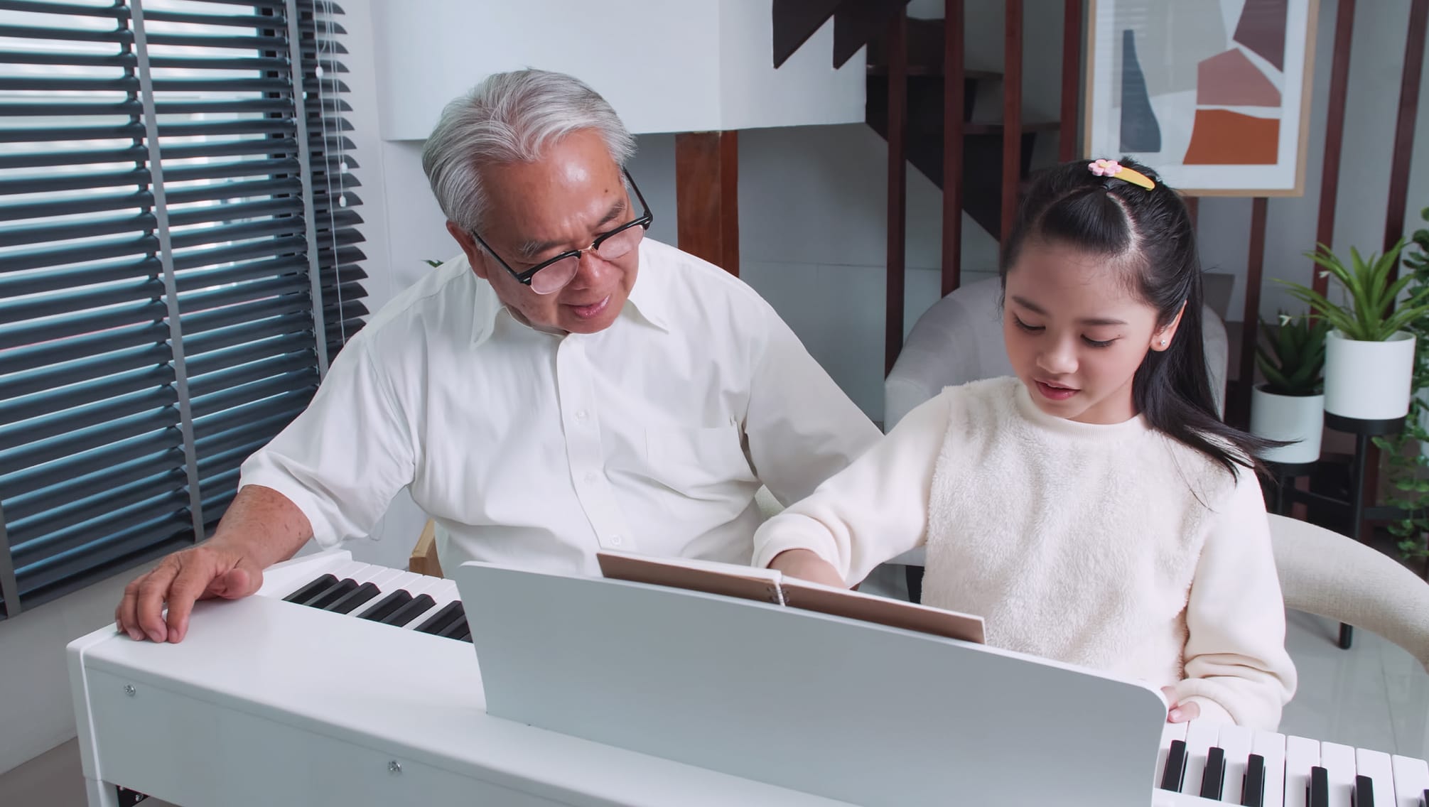 Grandfather is teaching little granddaughter play piano